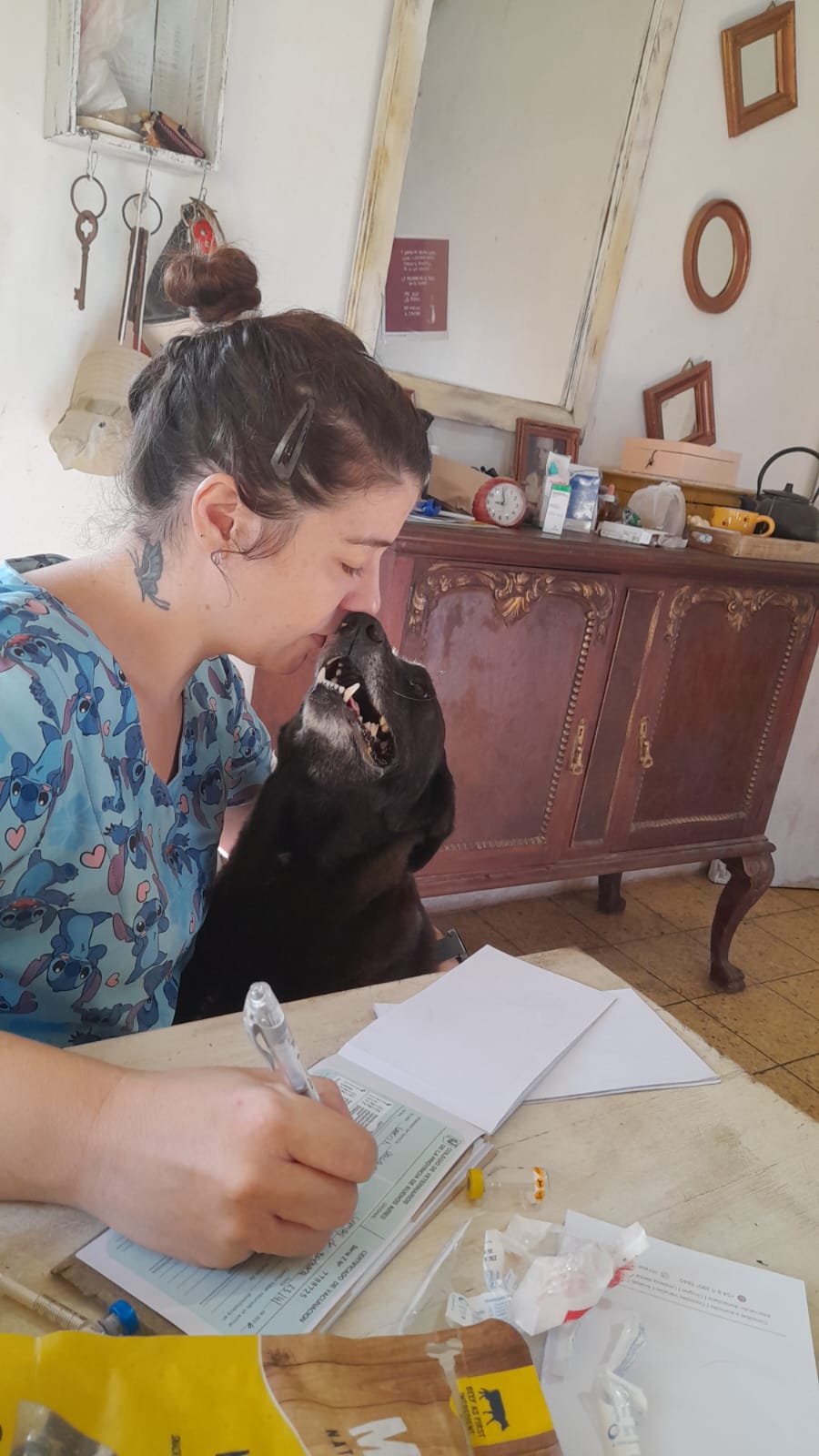 Jésica completando un certificado mientras un perro le acerca el hocico a la cara